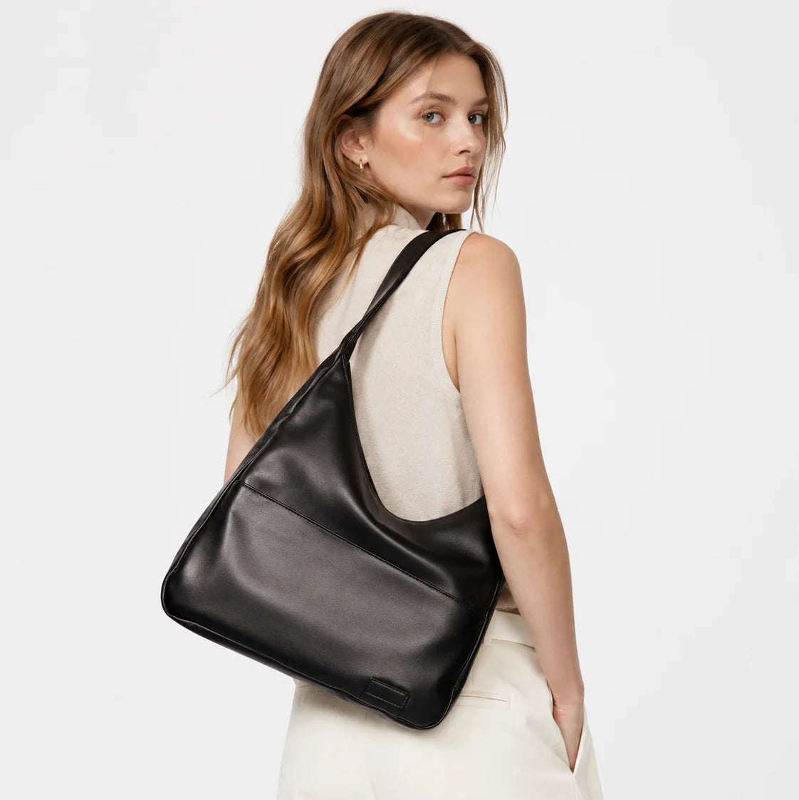 Woman carrying a black leather shoulder bag on a plain background